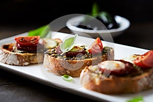 Crostini with tomato, salami and olive pesto on wooden background.