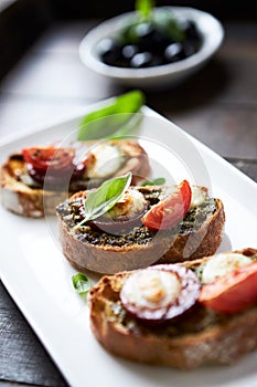 Crostini with tomato, salami and olive pesto on wooden background.