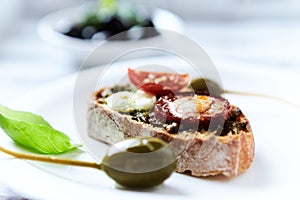 Crostini with tomato, salami and olive pesto on wooden background.