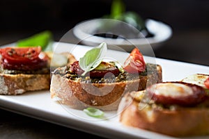 Crostini with tomato, salami and olive pesto on wooden background.