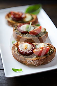 Crostini with tomato, salami and olive pesto on wooden background.