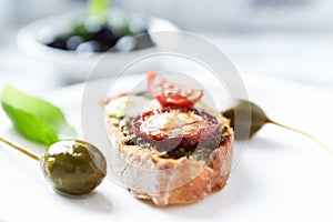 Crostini with tomato, salami and olive pesto on wooden background.