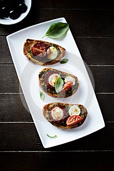 Crostini with tomato, salami and olive pesto on wooden background.