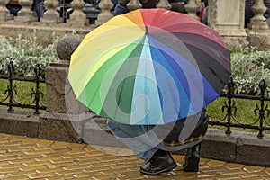 Crouched man under rainbow umbrella