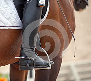 Croup of a red horse with a white saddle and a riderâ€™s foot in a boot with a spur inserted in a stirrup