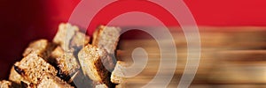 Croutons from black bread on red background. Delicious Fried crunchy crackers. Shallow depth of field image. Food panoramic banner