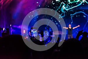 Crowd at concert. People silhouettes on backlit by bright blue and purple stage lights. Cheering crowd in colorful stage lights. R