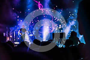 Crowd at concert. People silhouettes on backlit by bright blue and purple stage lights. Cheering crowd in colorful stage lights. R