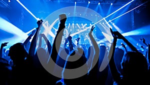 crowd dancing with neon blue lasers. People dancing at party with hands up. Silhouette crowd rejoices under bright stage lights at