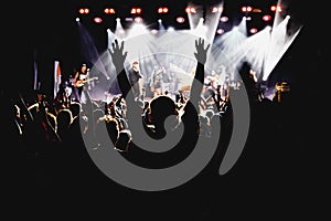 A crowd of happy people raising up hands at an open-air rock concert.
