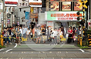 A crowd of Japanese pedestrians wait at a railroad crossing beneath colorful signs.