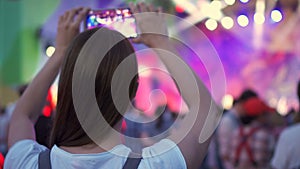 Crowd partying at open air rock concert. Woman standing, holding smartphone in hands shooting video