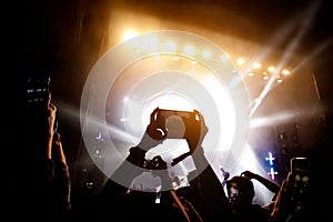 Crowd of people having fun while watching concert show at music festival. Raised hands with mobile phones