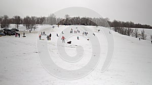 A crowd of people ride on snow slides. Children list themselves on the ice slide on inflatable rings. sledges, plastic