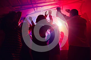 A crowd of people in silhouette raises their hands against colorful neon light on party background