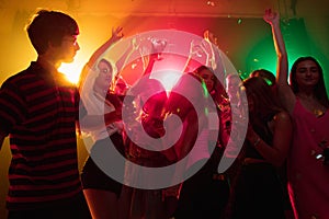 A crowd of people in silhouette raises their hands on dancefloor on neon light background