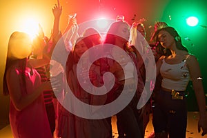 A crowd of people in silhouette raises their hands on dancefloor on neon light background