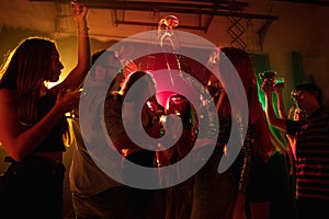 A crowd of people in silhouette raises their hands on dancefloor on neon light background