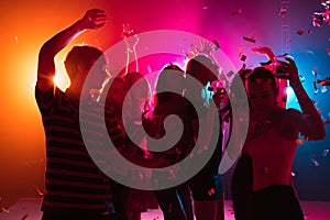 A crowd of people in silhouette raises their hands on dancefloor on neon light background