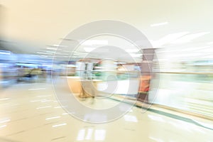 Crowd rushing inside a modern wide bright mall hall with boutiques, glass display windows, people in motion blur