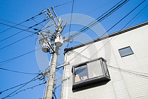 Crowded electrical pole with cords next to a white building with a window