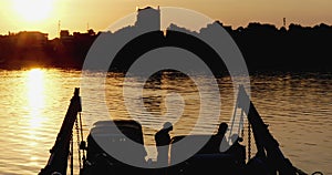 Crowded local ferry, brimming with passengers and cars, approaches the riverbank as the sky explodes in a sunset.