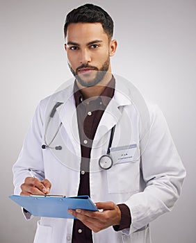 A crowded space and no mask Tsk Tsk. a handsome young doctor standing alone in the studio and writing on a clipboard.