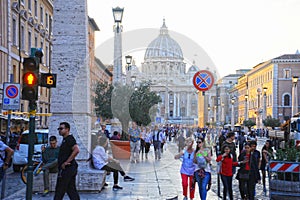 Crowds of people walk near the St Peter`s Basilica at the sunset in Rome, Italy. St Peter`s cathedral in Vatican City is one of