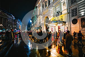 Crowds strolling down a rain-soaked street at night near Piccadilly Circus, London, UK