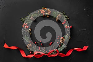 Crown of Christmas tree branches, pine cones, berries, and red slack, on black stone background