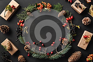 Crown of Christmas tree branches, pine cones, berries, walnuts, gifts, on black stone background