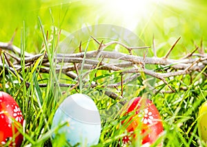 Crown of thorns and colorful eggs in green grass at sunny day. Easter background