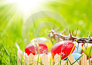 Crown of thorns and colorful eggs in green grass at sunny day. Easter background