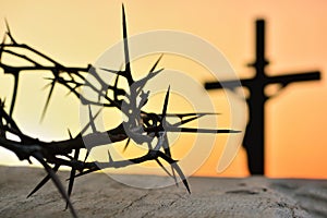 Crown of thorns of Jesus Christ against silhouette of catholic cross at sunset background