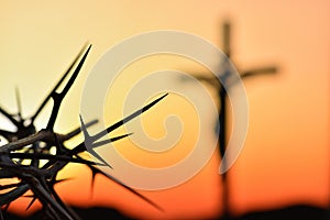 Crown of thorns of Jesus Christ against silhouette of catholic cross at sunset background