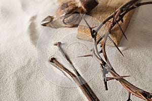 Crown of thorns, wooden plank and hammer with nails on sand. Easter attributes