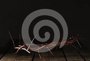 Crown of thorns on wooden table against dark background  space for text. Easter attribute