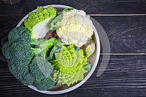 Cruciferous vegetables. Romanesco, cauliflower and broccoli on a round tray on a wooden background. Flat lay. Top view