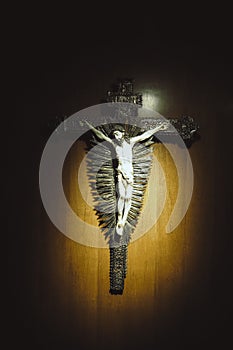 Crucifixion of Jesus pendant hang on brown wood wall with spot light to the crucify cross