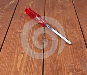 Cruciform screwdriver with the red handle on wooden surface