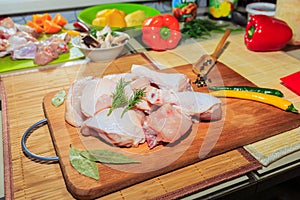 Crude chicken meat on a kitchen table, vegetables and kitchen accessories lie nearby