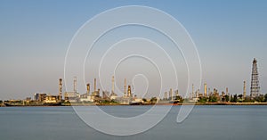 Crude oil refinery plant and many chimney with petrochemical tanker or cargo ship at coast of river on sky afternoon  bright day