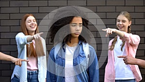 Cruel group of teens pointing fingers at curly afro-american schoolgirl, racism