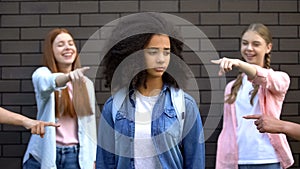 Cruel group of teens pointing fingers at curly afro-american schoolgirl, racism photo