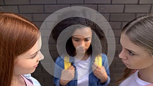 Cruel schoolgirls looking each other, scared black classmate background, abuse