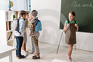 Cruel schoolkids gossiping and laughing near