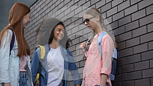 Cruel teenagers pushing with elbow shy classmate in eyeglasses school backyard