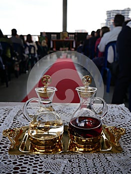 Cruets with water and wine ready for catholic mass with red carpet and people in the background