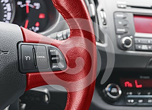 Cruise control buttons on the red steering wheel of a modern car, car interior details.