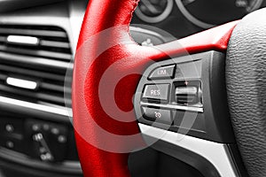 Cruise control buttons on the red steering wheel of a modern car, car interior details.